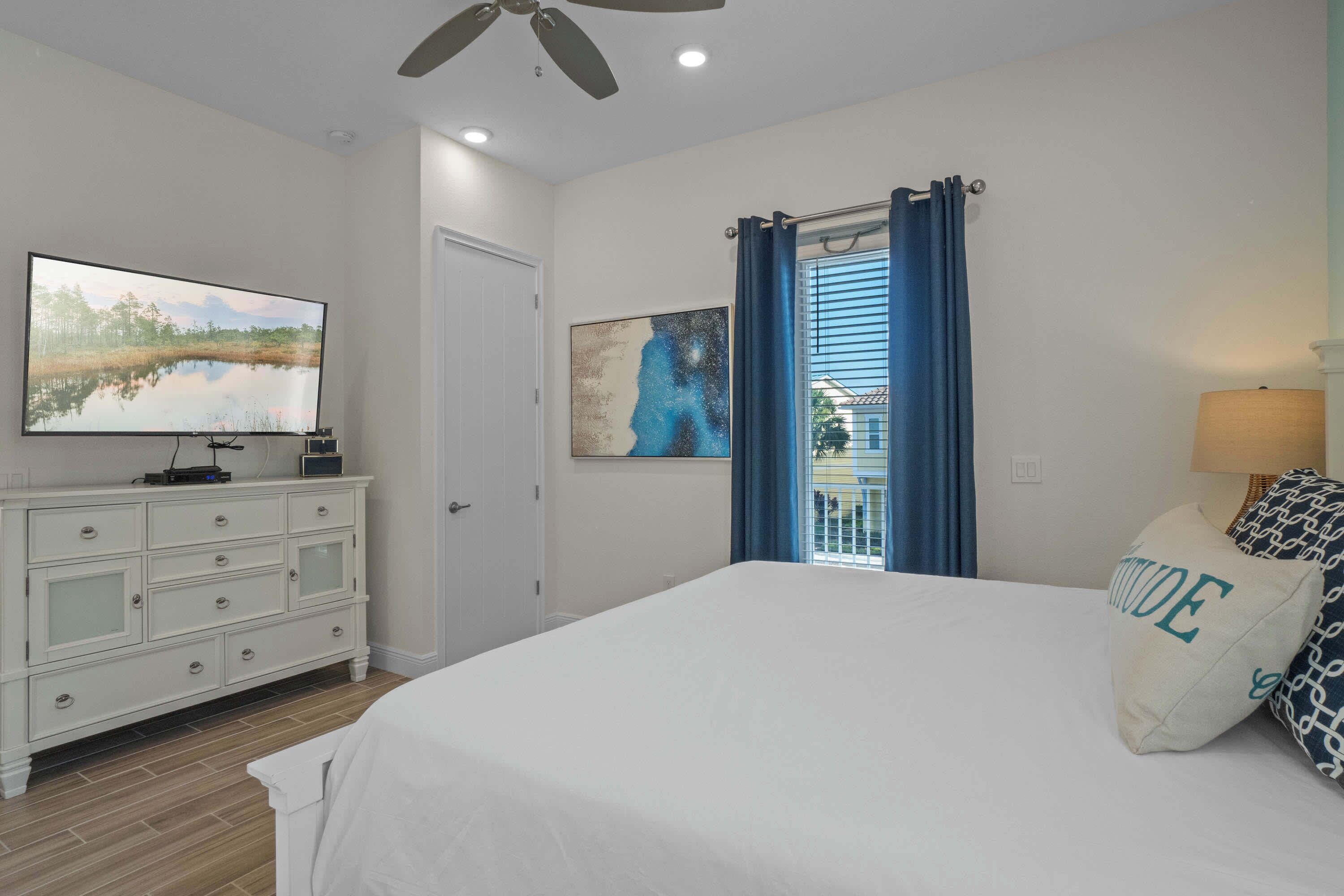 A bedroom with a bed, a dresser, a television, and artwork on the walls.
