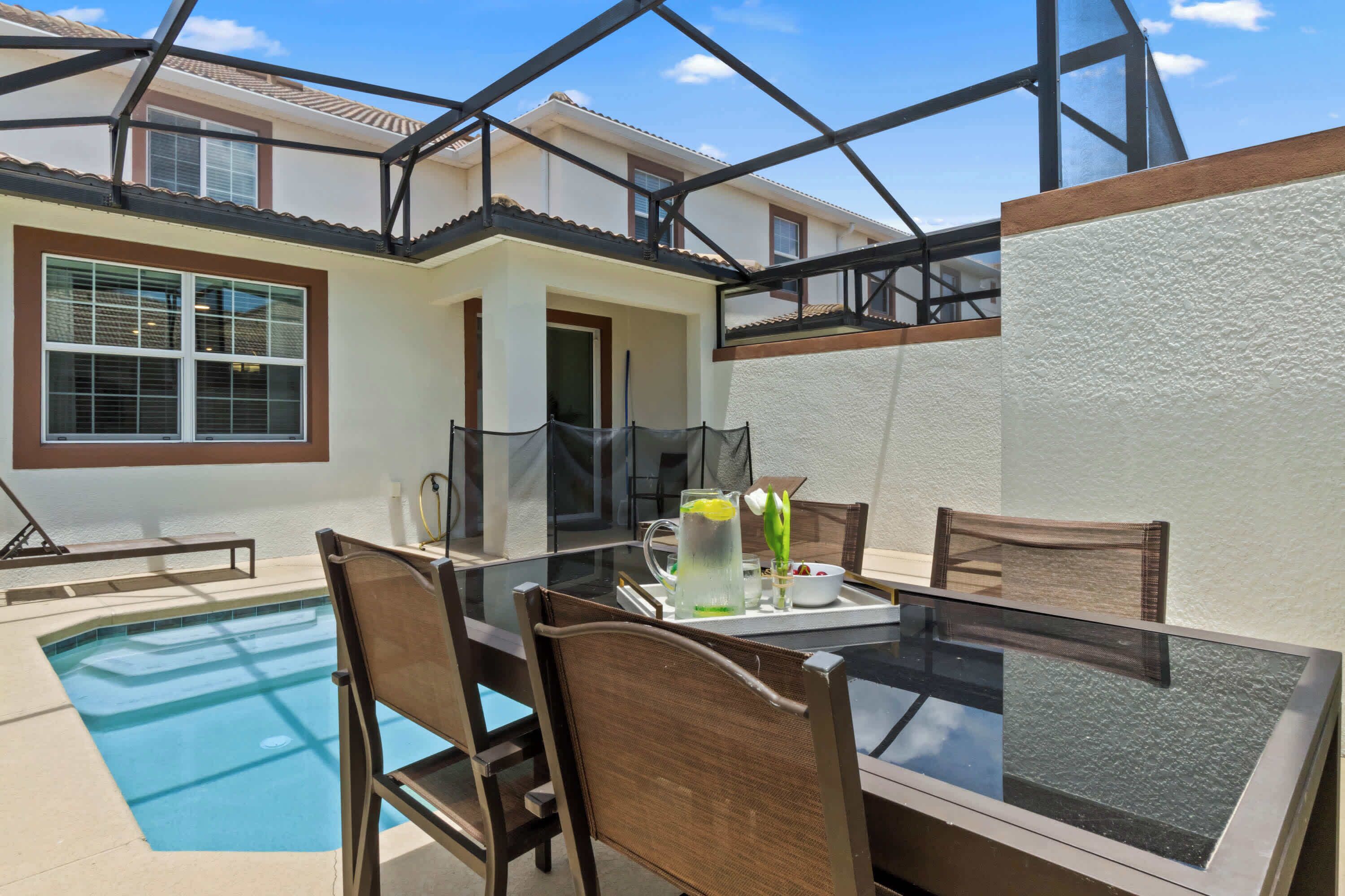 Une table avec un plateau en verre, des chaises, une piscine et un patio couvert.