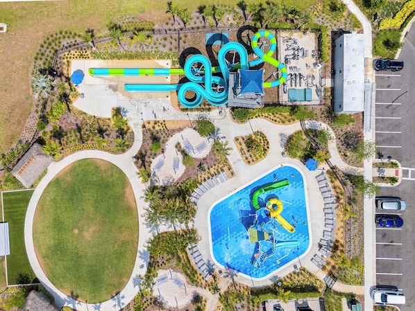 Luftaufnahme eines Wasserparks mit großem Pool, Rutschen und einem Parkplatz.