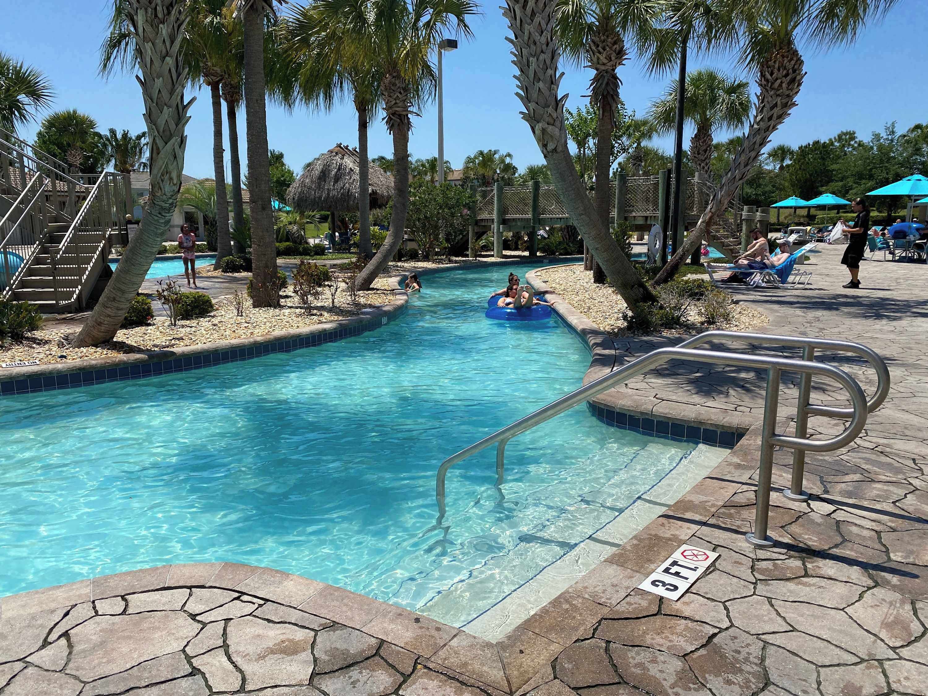 A swimming pool with clear blue water, surrounded by palm trees and lounge chairs.