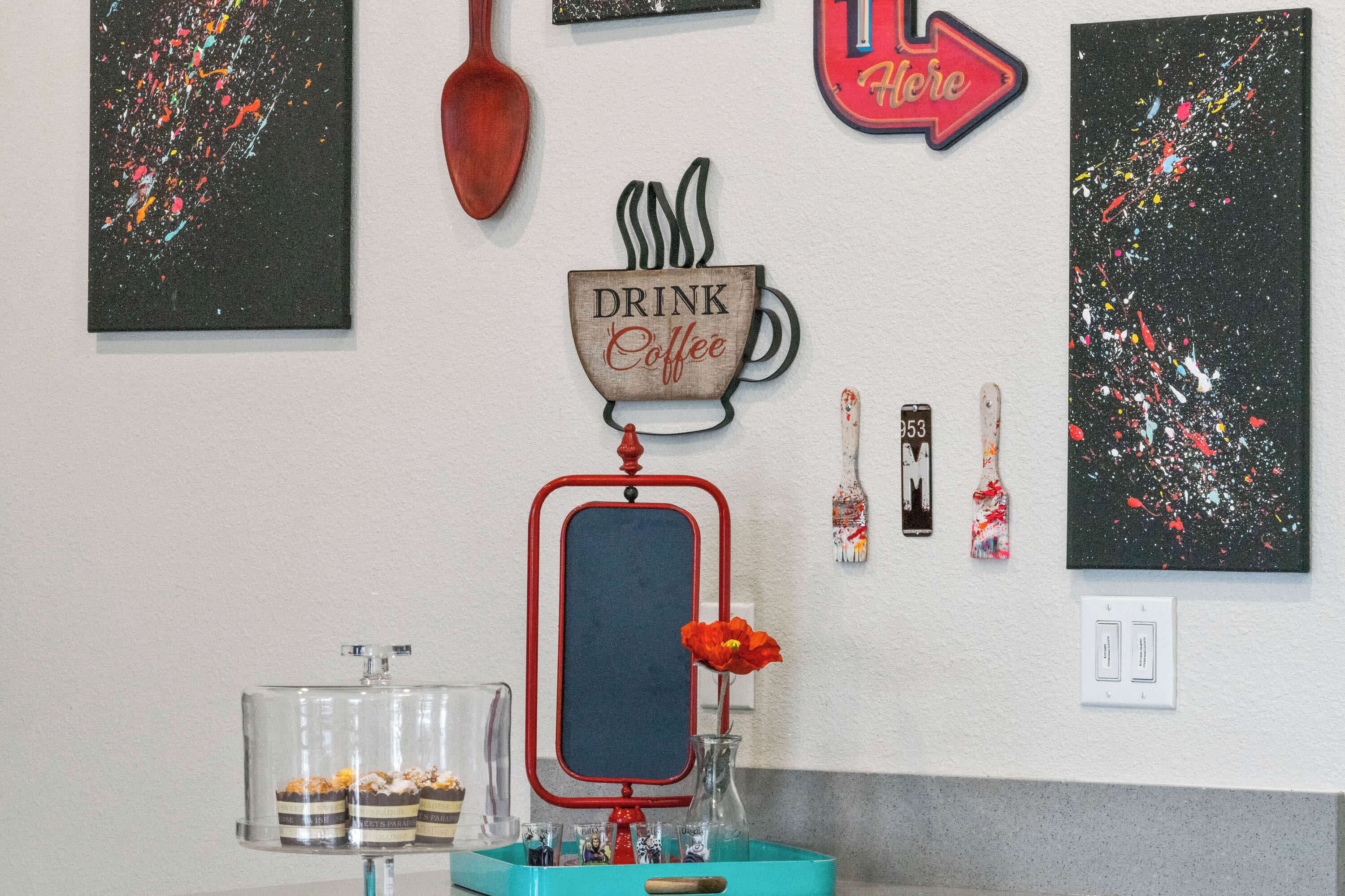 A wall with a coffee cup sign, a mirror, and abstract art.