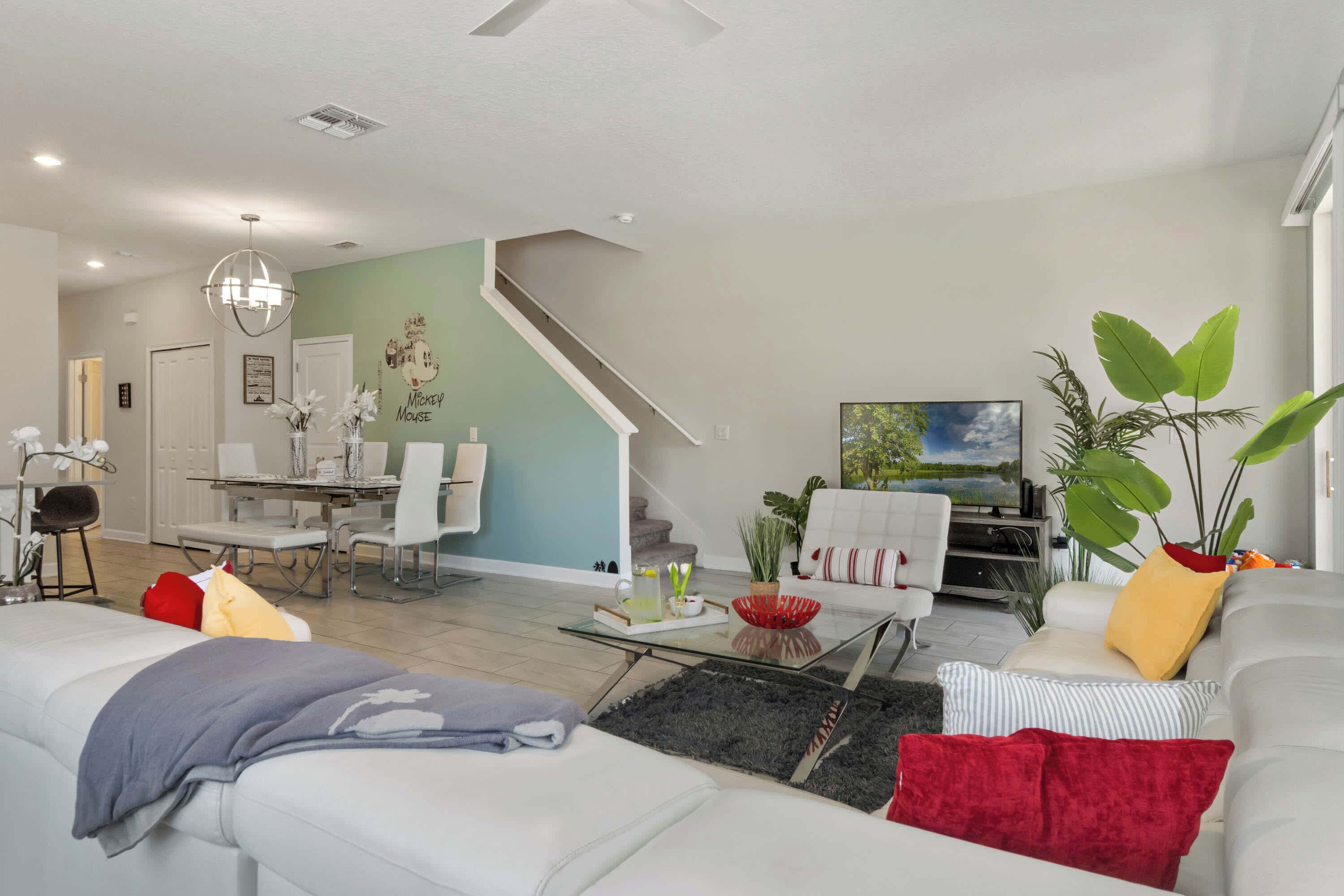 A modern living room with a sofa, coffee table, and a TV. There is a staircase leading to another room.