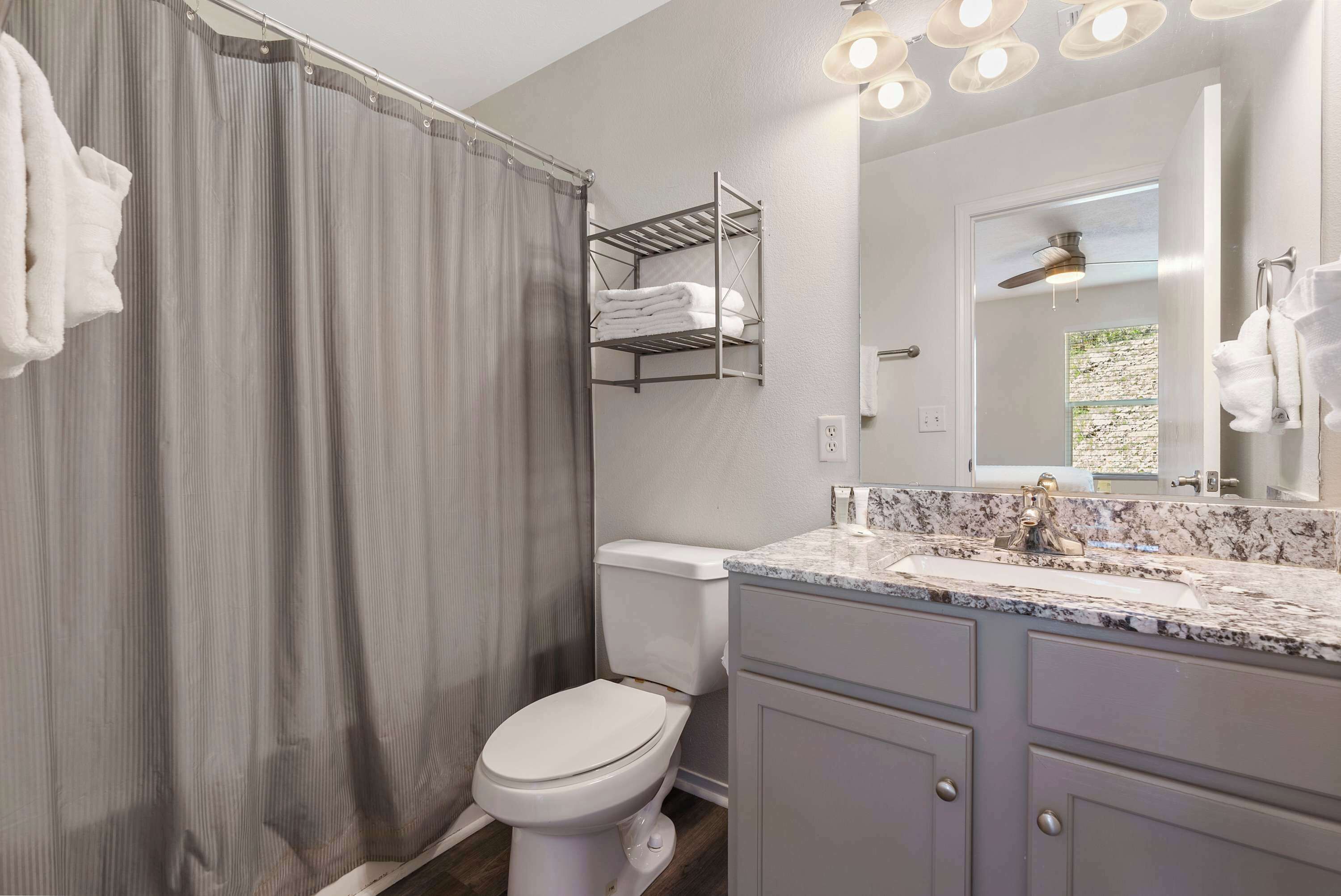A bathroom with a shower curtain, a toilet, a sink with a marble countertop, and a towel rack.