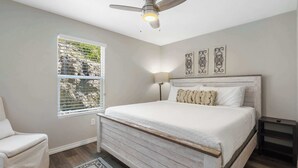 Ein Schlafzimmer mit einem Bett, einem Sessel, einem Fenster mit Jalousien, einem Deckenventilator und Wandbildern.