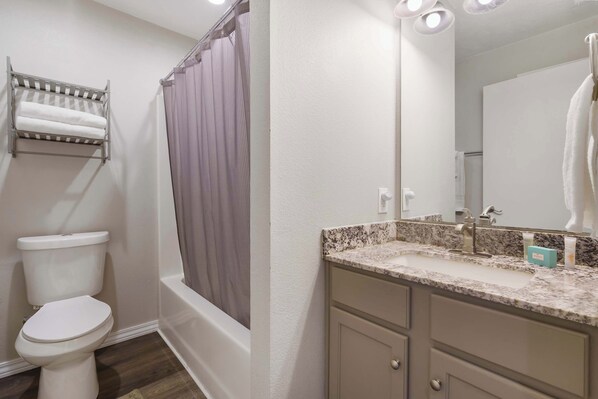 A bathroom with a toilet, a shower with a curtain, a sink with a mirror, and a towel rack. - Hillside Lodge - Enjoy Music Venues & the Open Air (Branson)