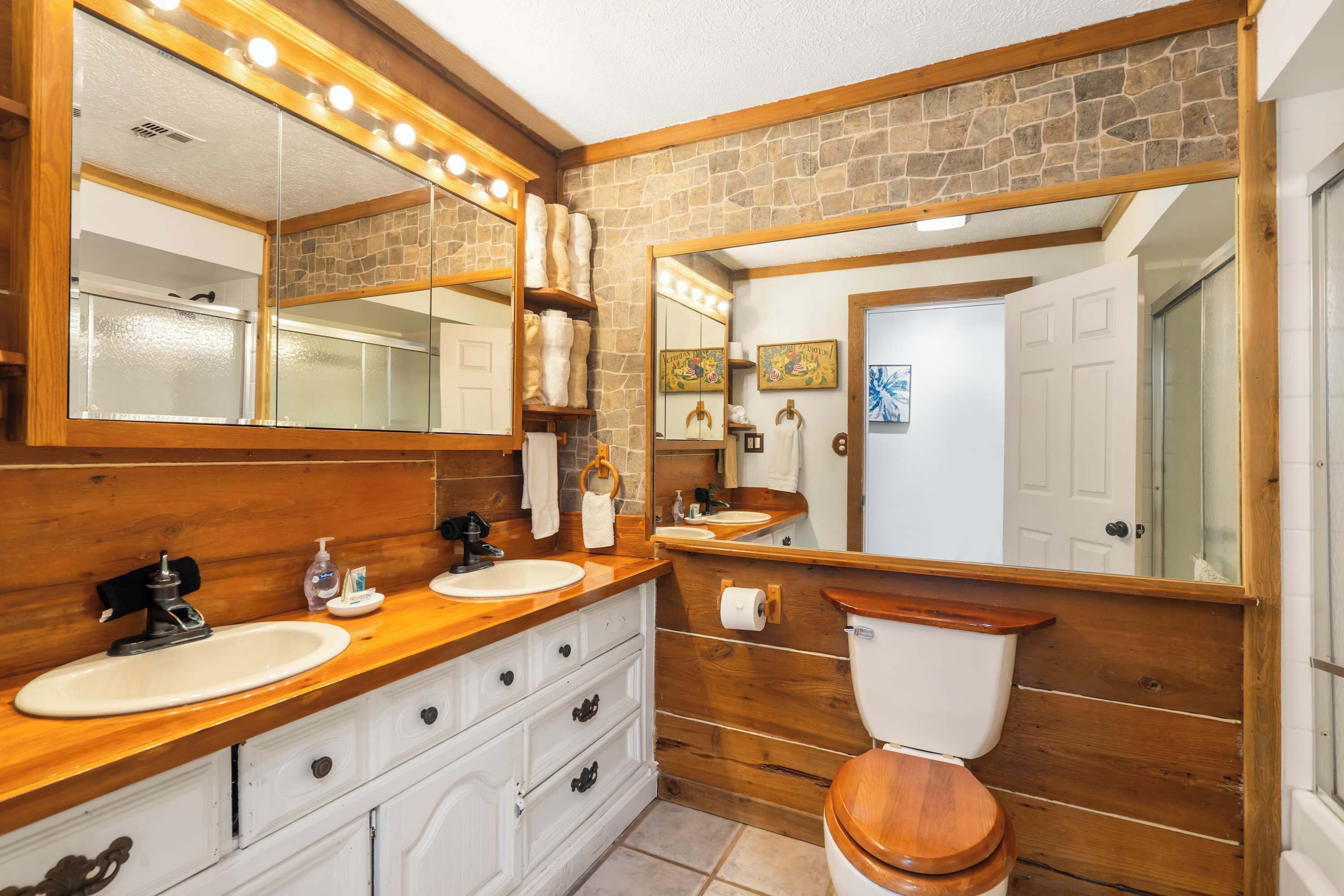 Un baño con tocador de madera, un espejo grande, inodoro y pared de piedra.