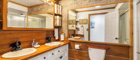 Un baño con tocador de madera, un espejo grande, inodoro y pared de piedra.