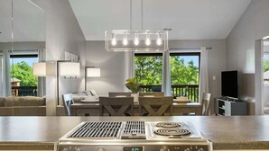 Een moderne keuken met een ingebouwde kookplaat, een eethoek met tafel en stoelen, en een groot raam met uitzicht op groen.