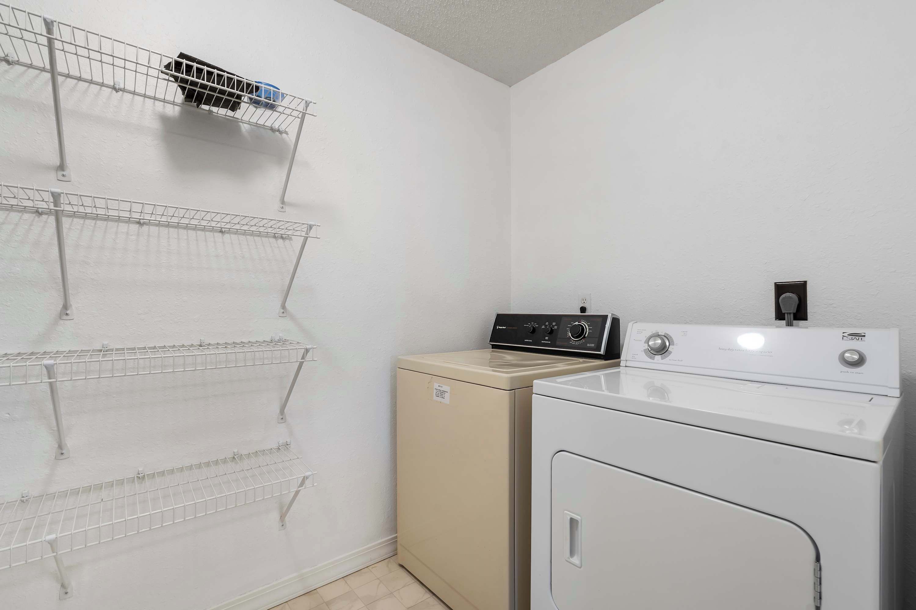 A laundry area with a washing machine and dryer, and three wire shelves mounted on the wall.
