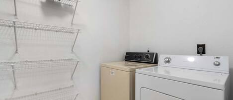 A laundry area with a washing machine and dryer, and three wire shelves mounted on the wall.