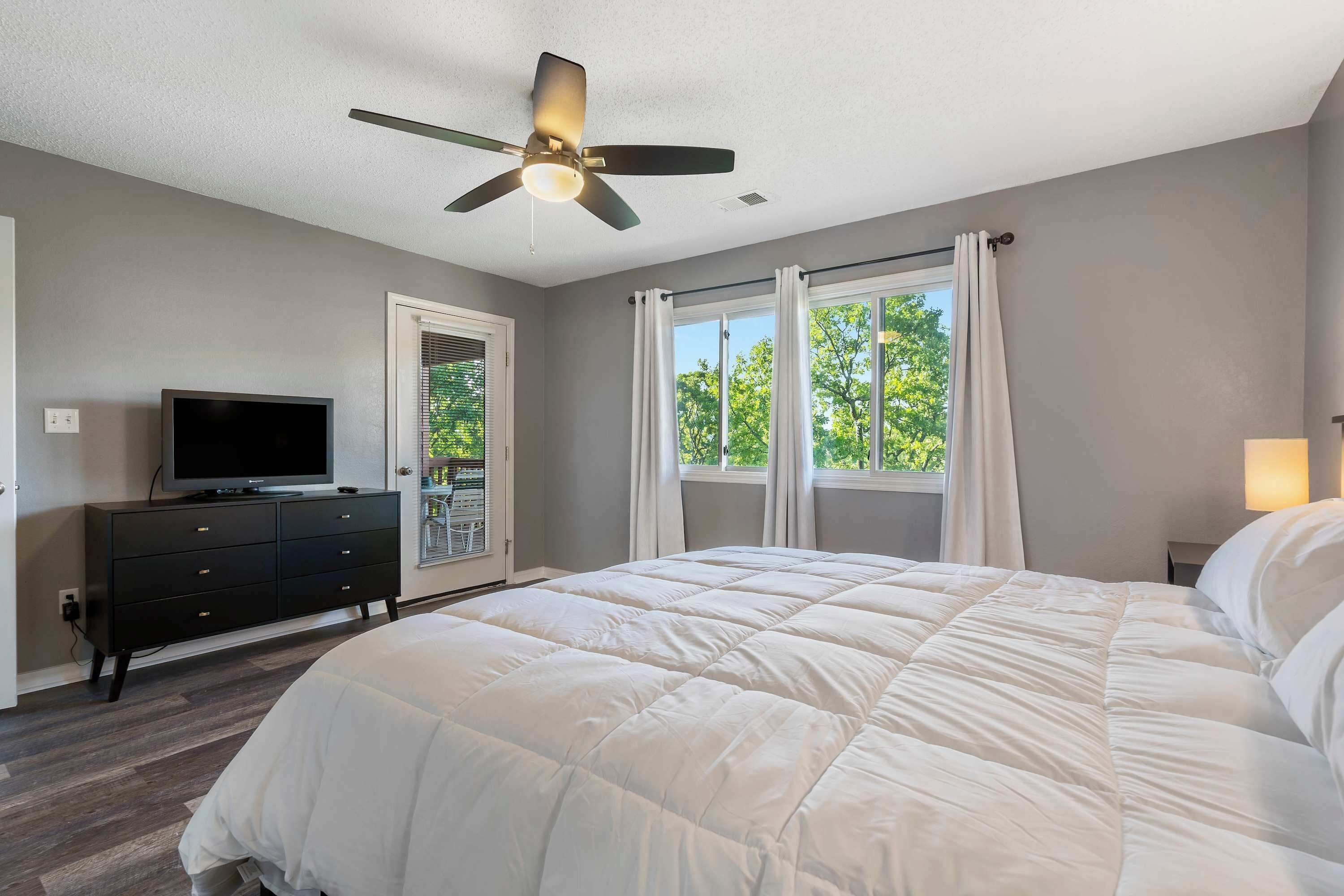 A bedroom with a bed, a ceiling fan, a TV on a dresser, and a window with curtains.