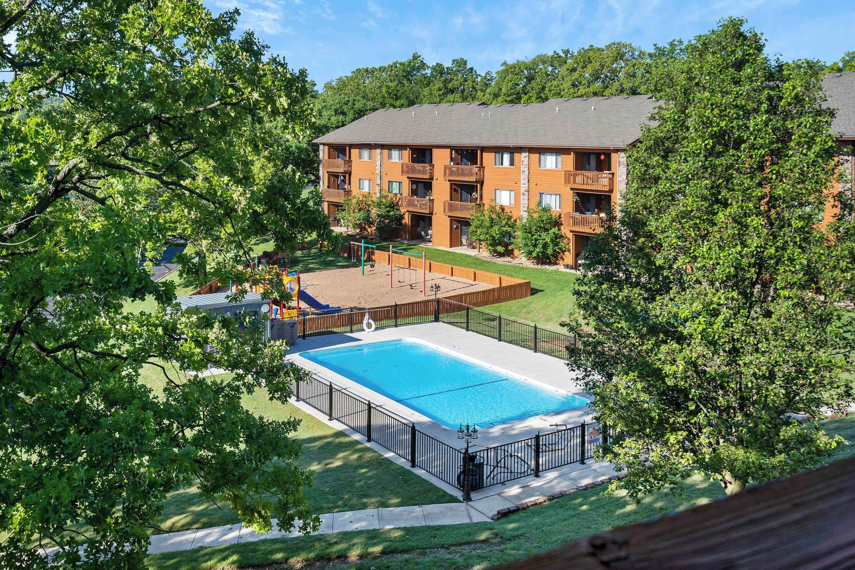 A residential building with a swimming pool, surrounded by trees and a fenced yard.