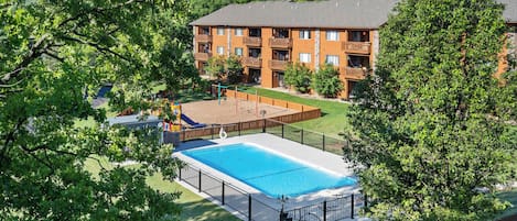 A residential building with a swimming pool, surrounded by trees and a fenced yard.