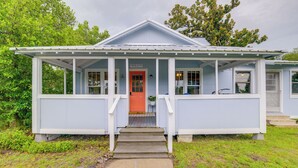 Una casa con un portico, una porta rossa e un piccolo giardino antistante.
