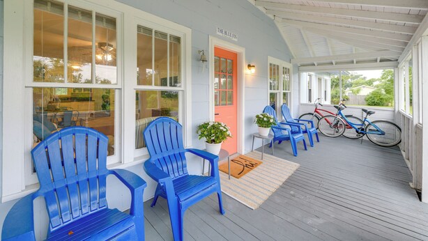 Un portico riparato con poltrone Adirondack blu, una porta rossa e biciclette.