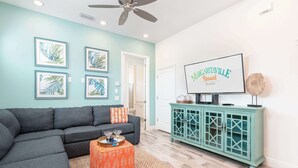 A living room with a teal wall, a gray sectional sofa, a teal cabinet, and framed artwork. - Shake Shack Heated Pool & Hot Tub (Kissimmee)