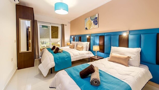 Une chambre d’hôtel avec deux lits, une grande fenêtre, une tête de lit bleue et un tableau au mur.