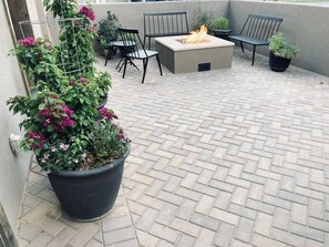 Relax by the fire pit in this serene outdoor patio area, surrounded by lush greenery and comfortable seating.