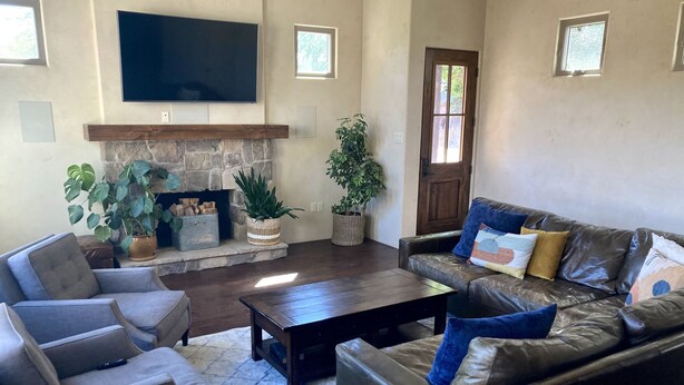 A living room with a stone fireplace, leather sofas, a coffee table, and a flat-screen TV mounted on the wall. - Custom built family home, close to balloon fiesta park  (Albuquerque)