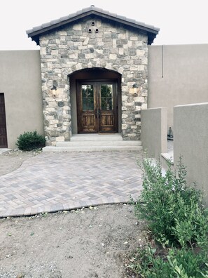 Stunning stone-clad building with a central entrance and steps, flanked by stone walls and surrounded by a charming garden.