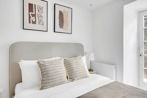 Relax in a serene space with a neatly made bed, grey headboard, and abstract artwork.