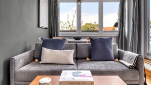 A grey sofa with two pillows, a book titled 'The Kinfolk Garden', and a wooden side table with a bowl and a lamp.