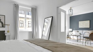 Een moderne hotelkamer met een groot bed, uitzicht op de stad door het raam, en een apart zithoekje met een bank en stoelen.