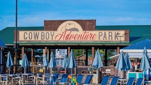 Un letrero para 'Cowboy Adventure Park' con un logotipo, una zona de estar cubierta con sombrillas azules y sillas reclinables.