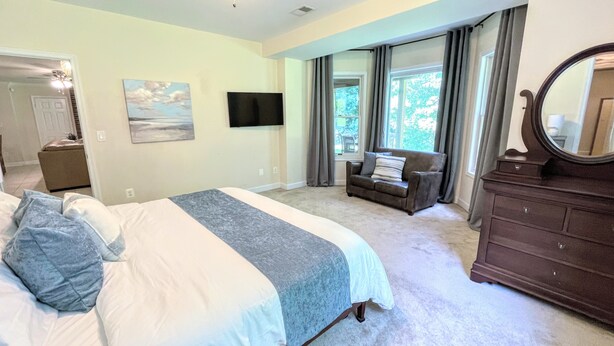 A bedroom with a large bed, a dresser, a TV, and a window with curtains.