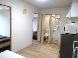 A compact hotel room with a bed, a small kitchenette, a toilet, and a shower area.