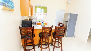 A compact kitchen with wooden cabinets, a refrigerator, and a dining area with three wooden chairs.