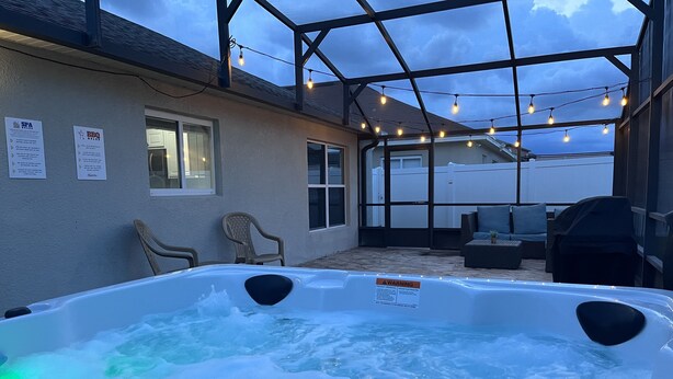 Un bain à remous agrémenté d’un panneau d’avertissement, de deux chaises et d’un patio couvert illuminé de guirlandes lumineuses.