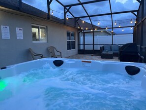 Un bain à remous agrémenté d’un panneau d’avertissement, de deux chaises et d’un patio couvert illuminé de guirlandes lumineuses.