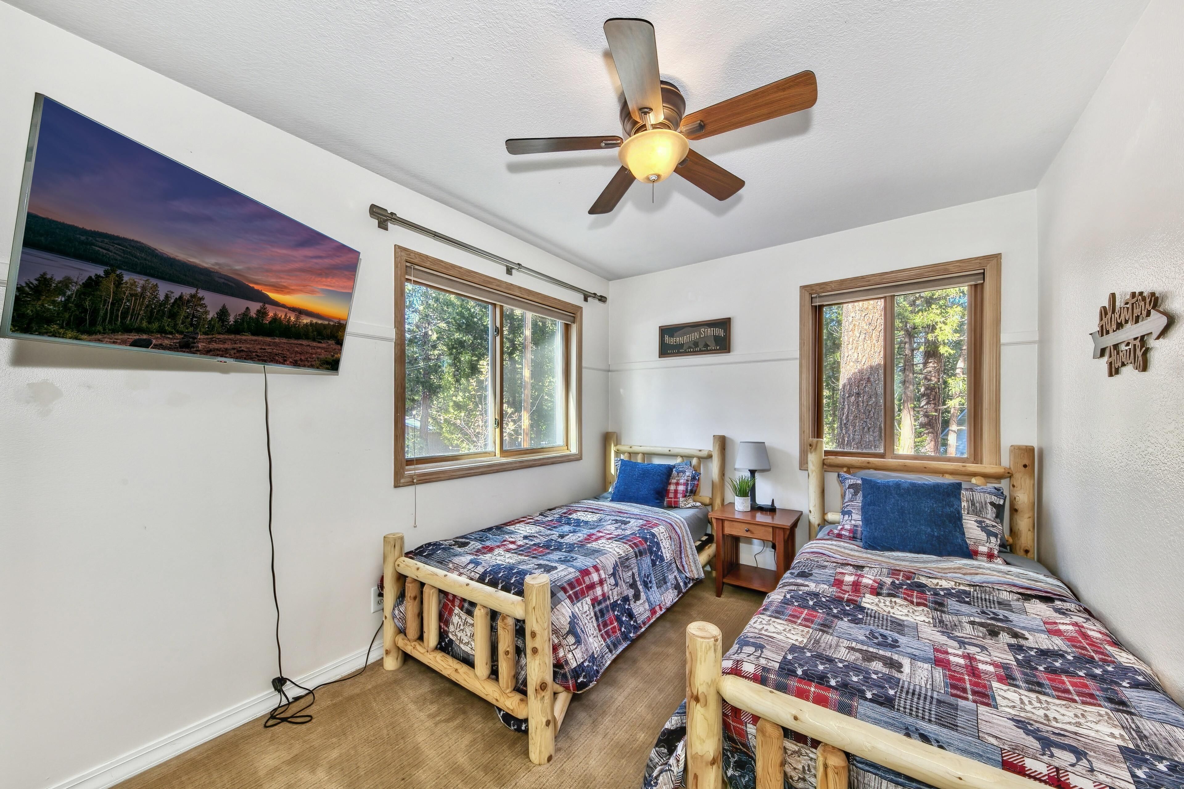 A bedroom with two wooden beds, a ceiling fan, and large windows.