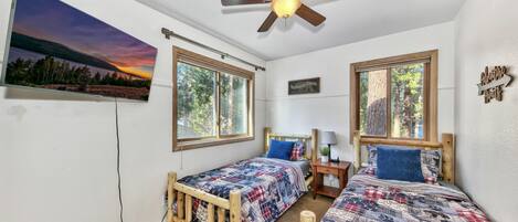 A bedroom with two wooden beds, a ceiling fan, and large windows.