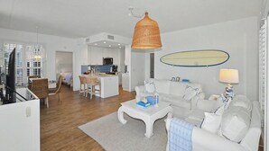 Ein modernes Wohnzimmer mit einem weißen Sofa, einem Couchtisch und einem Essbereich mit Korbstühlen.