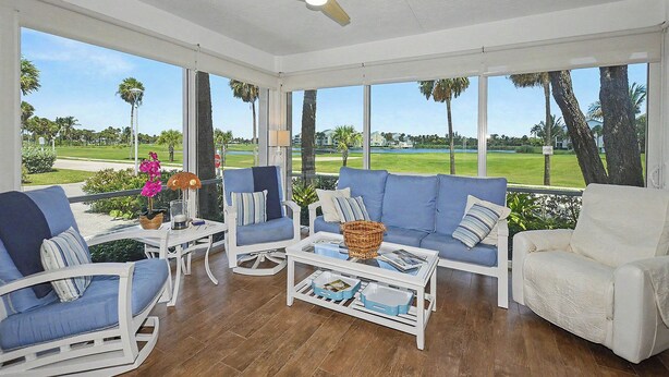 Ein Wintergarten mit Blick auf einen Golfplatz, ausgestattet mit einem weißen Deckenventilator, einem blauen Sofa und einem weißen Sessel.