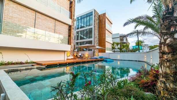 A modern pool area with a clear pool, surrounded by lush greenery and palm trees.