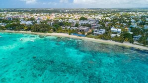 An aerial view of a coastal town with clear turquoise waters, a sandy beach, and residential buildings.