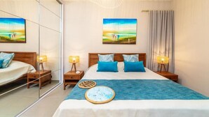 A hotel room with a large bed, two bedside tables with lamps, a mirror, and two paintings on the wall.