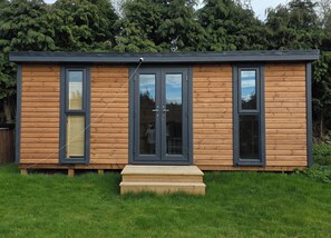 Une cabane moderne en bois, dotée de grandes fenêtres, d’une terrasse en bois et offrant une vue sur la forêt environnante.