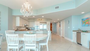 A spacious kitchen with white cabinetry, a dining area with white chairs, a chandelier, and a large island with a sink. - Three Bedroom Condo with Gorgeous Beach Views! Complimentary Boat Slip! (Orange Beach)
