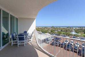 Ein Balkon mit Tisch und Stühlen, ein Parkplatz und Blick auf das Meer und Palmen.