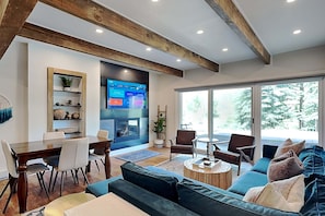 A modern living room with a dining area, a fireplace, and large windows offering a view of trees. - 🌲Timberline D1D Deluxe 2-Bedroom ~Hot Tub~Pool~WiFi~Ski-in/out~Local Shuttle🌲 (Snowmass Village)