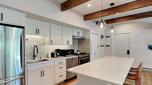 Una cocina moderna con armarios blancos, electrodomésticos de acero inoxidable, una isla grande y vigas de madera.