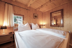 Una habitación con paneles de madera, una cama, una mesita de noche, una lámpara, una ventana y un espejo.