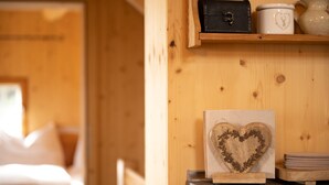 Ein Holzinnenraum mit einem Bett, einer herzförmigen Holzdekoration und einem Regal mit einer schwarzen Tasche, einem weißen Behälter und einer Vase.