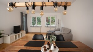 A modern dining area with a wooden table, black mats, a white vase with pinecones, and a bottle of wine. - Apartment 'LO Ferienwohnung' with Terrace & Wi-Fi (Friedrichshafen)