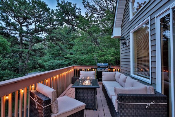 Relax on the deck with a grill and fire pit, surrounded by string lights and a forest view.