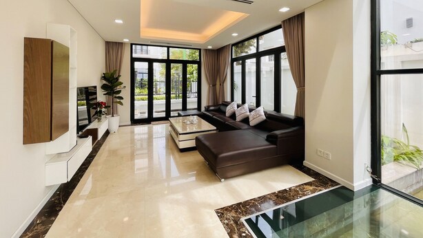 A modern living room with a sectional sofa, a glass coffee table, and a flat-screen TV mounted on the wall.